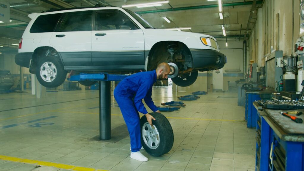 Free A Man in Blue Coveralls Holding a Tire Stock Photo