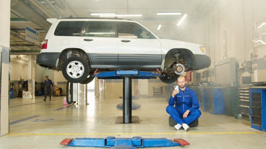 Free A Man in Coveralls Sitting on a Black Tire Holding a Smartphone Stock Photo