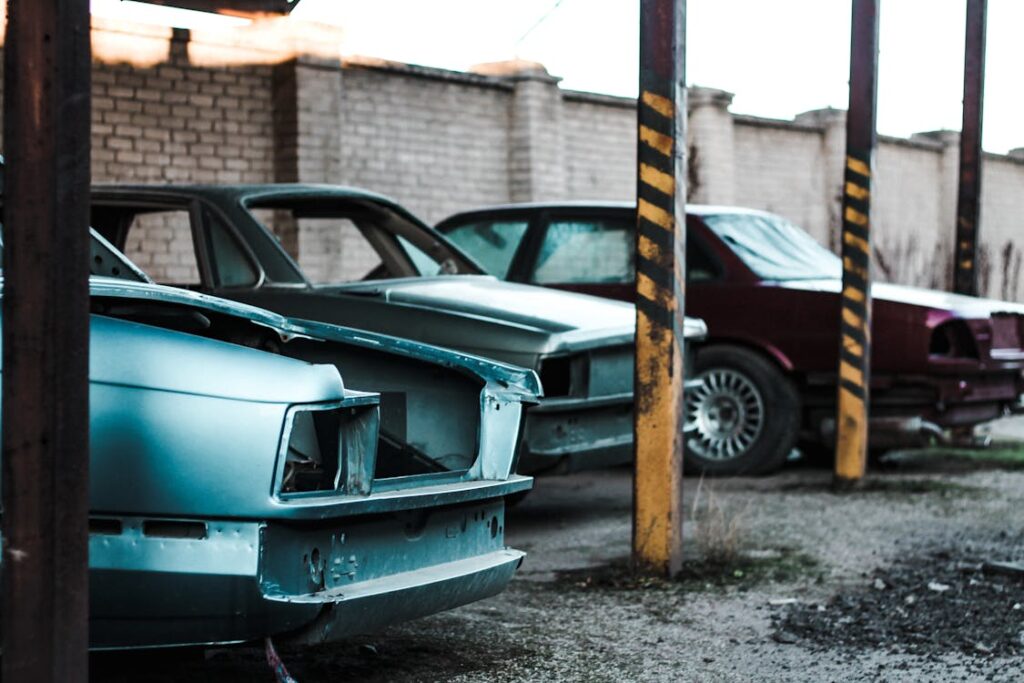 Free Various old fashioned derelict broken automobiles placed on parked lot near stone fence and metal posts on street in city Stock Photo